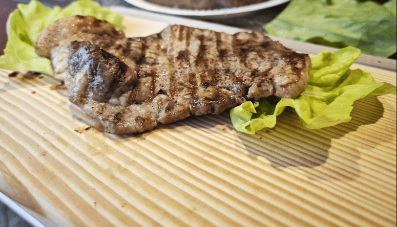 Grilled meat with char marks served on lettuce leaves over a light wooden board.