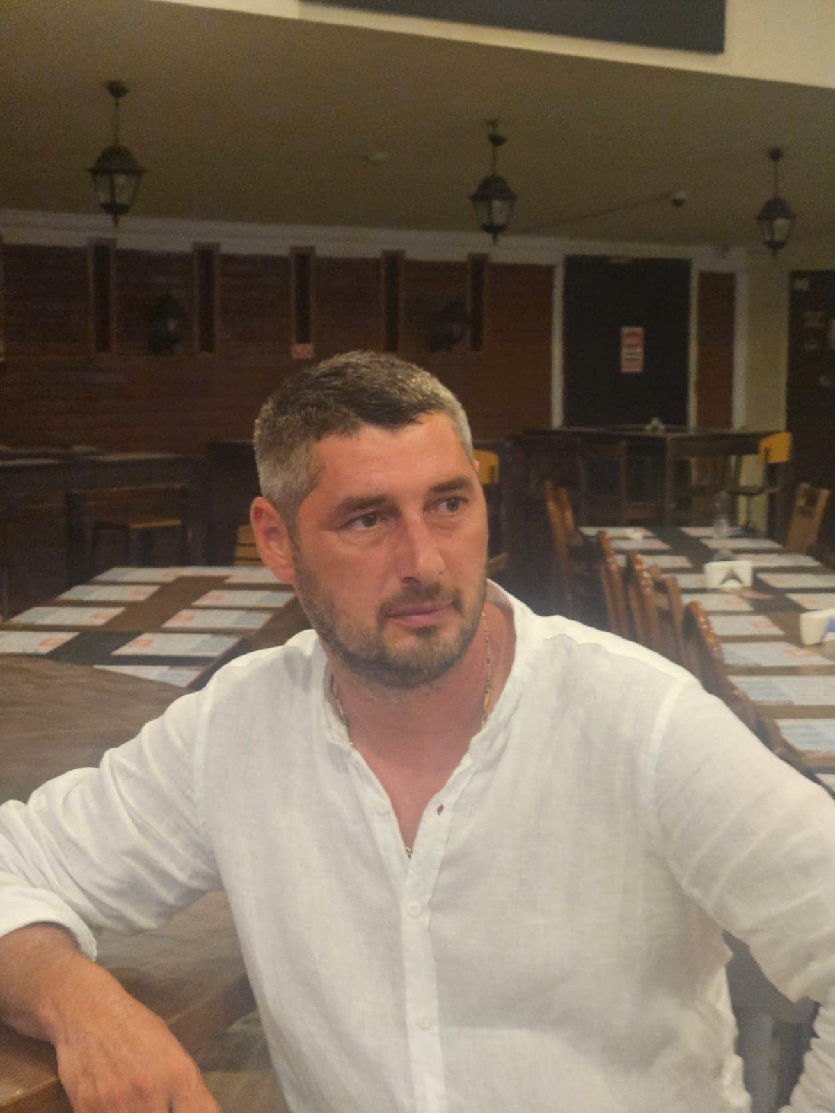 Bearded man in a white linen shirt sitting at a table in a restaurant.