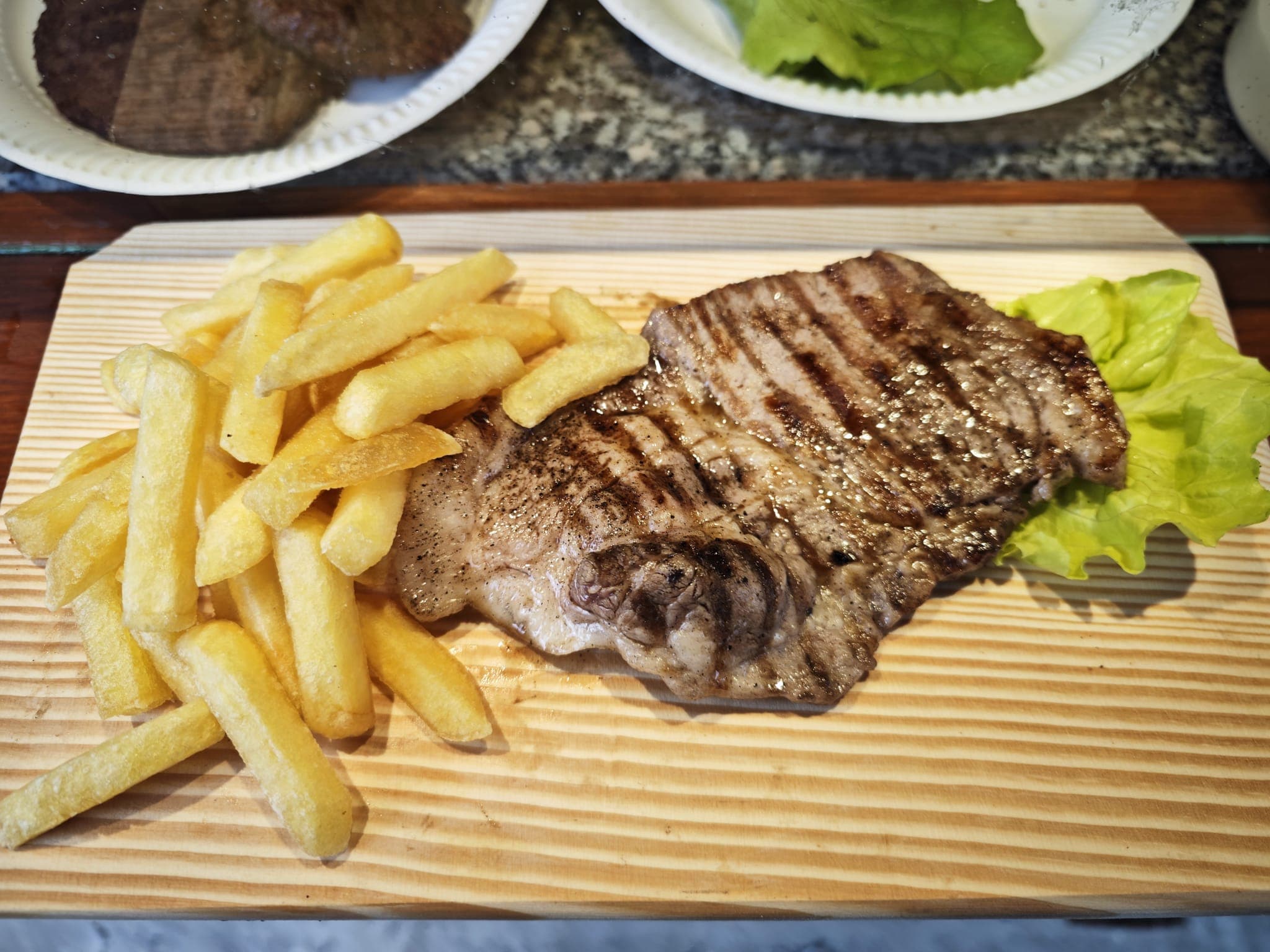Grilled steak with char marks and golden french fries served on a wooden board.