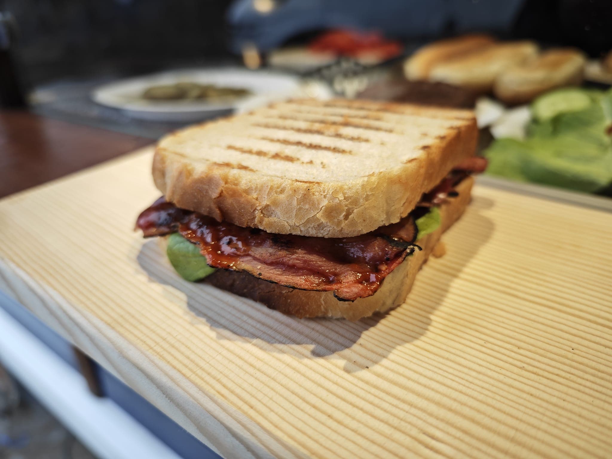 Grilled sandwich with thick-cut glazed meat and lettuce on a light wooden cutting board.