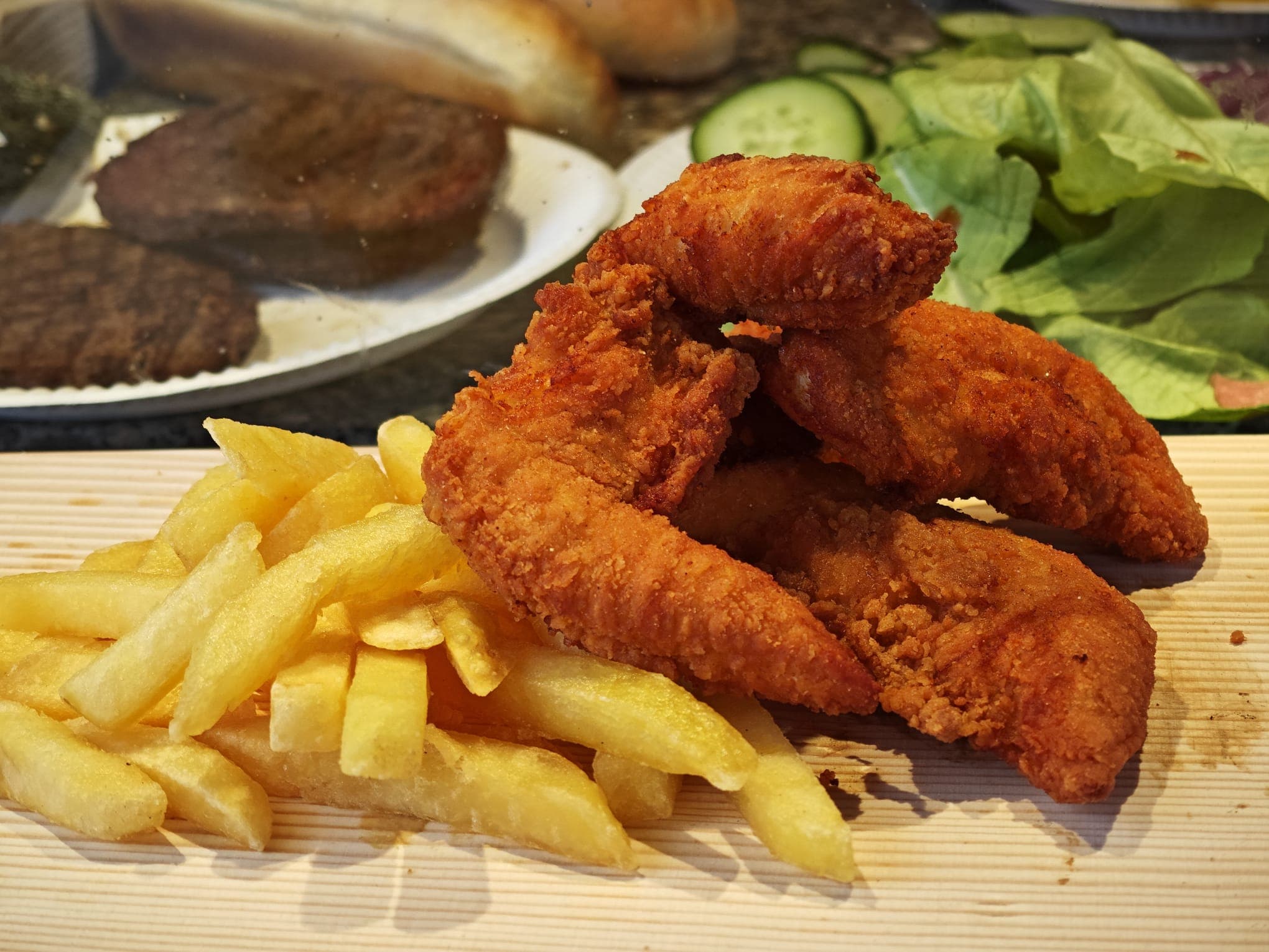 Crispy breaded chicken tenders and golden French fries served on a light wooden board.